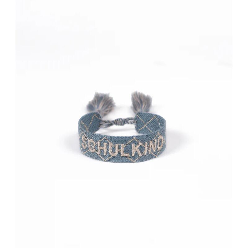leevjearmband2 Blue woven bracelet with white embroidery forming a geometric pattern and the word SHULKND, with two tassels at ends.